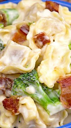 a blue bowl filled with pasta and broccoli covered in cheese, bacon and other toppings