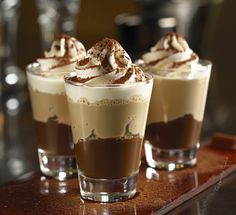 three glasses filled with different types of desserts on a table together and topped with whipped cream