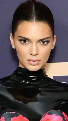 a woman with dark hair wearing a black top and pink flowers on her body is looking at the camera