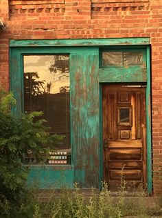 an old green door and window in front of a brick building with plants growing outside