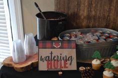 a table topped with cupcakes next to a sign that says watering hole