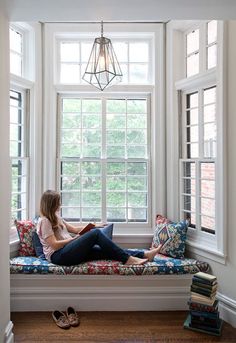 a woman sitting on a window sill reading a book