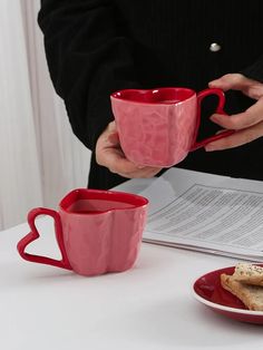 two red coffee mugs sitting on top of a table next to a plate of food