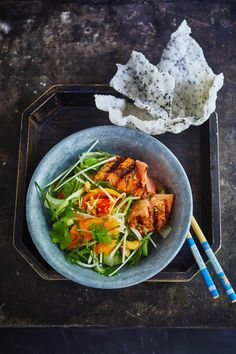 a bowl filled with meat and veggies next to chopsticks on a tray