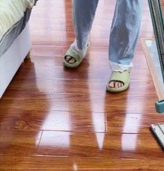 a person standing next to a bed on a hard wood floor with their feet propped up