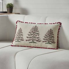 a christmas tree pillow sitting on top of a couch next to a white sofa with red pom - poms