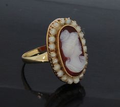 Antique 14 carat gold ring with shell cameo and a frame of blister pearls. This 14 karat yellow gold ring is handmade and is in a beautiful antique condition. There are traces of glue on the pearls (see photo), but a beautiful item of jewelery for the collector or enthusiast. ▶ Ring size is 17 (53) ▶ Weight is 4 grams ▶ Ring head is 20x14mm ▶ Gold mark 585 ▶ Dutch hallmarked (Oak leaf) ▶ Condition: beautiful antique condition Comes in a jewelery box, well packaged and shipped insured. Elegant White Cameo Ring, Elegant Cameo Rings, Fine Jewelry Cameo Wedding Ring, Fine Jewelry Cameo Rings For Weddings, Wedding Cameo Ring In Yellow Gold, Wedding Yellow Gold Cameo Ring, Yellow Gold Cameo Ring Fine Jewelry, White Cameo Rings For Wedding, 14k Gold Cameo Rings For Wedding