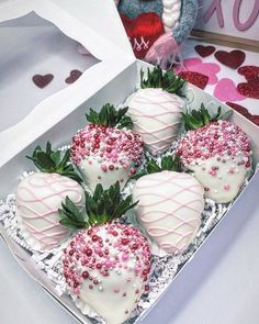 four chocolate covered strawberries with sprinkles in a white box next to a teddy bear