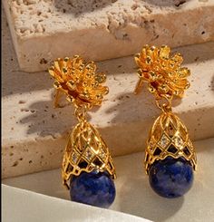 LAPIS LAZULI BLOOM EARRINGS Lustrous Gemstones: The Lapis Lazuli Bloom Earrings feature a design inspired by the delicate beauty of blooming flowers. At the heart of each earring, the deep blue Lapis Lazuli gemstones, known for their association with inner wisdom and truth, take center stage. Surrounding them is a meticulously crafted flower detail in 18K gold plated stainless steel, adding a touch of floral grace and sophistication to the design. Delicate Flower Detail: Lapis Lazuli Bloom Earri Elegant Sapphire Earrings With Natural Stones, Blue Elegant Flower Earrings For Formal Occasions, Elegant Blue Pierced Flower Earrings, Elegant Blue Flower Drop Earrings, Elegant Blue Flower Earrings As Gift, Elegant Blue Flower Earrings For Gift, Elegant Flower Shaped Jewelry With Gemstone Accents, Elegant Flower-shaped Jewelry With Gemstone Accents, Elegant Sapphire Flower Jewelry