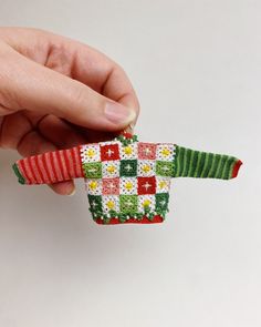 a hand is holding an ornament that looks like a christmas sweater with flowers on it