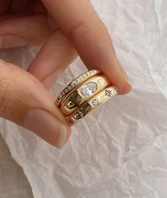 a woman's hand holding two gold rings with diamonds on each one and the other