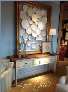 a table with plates on it in front of a mirror and lamp next to a couch