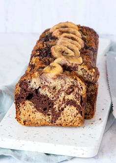 a loaf of chocolate banana bread on a white platter next to a knife and napkin