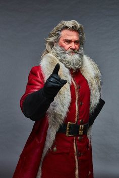 a man dressed as santa claus giving the thumbs up sign with his hand and wearing a red coat