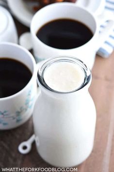 two cups of coffee sit next to each other on a table with pastries in the background