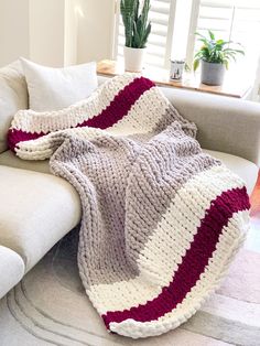 a couch with a blanket on top of it next to a potted plant and window