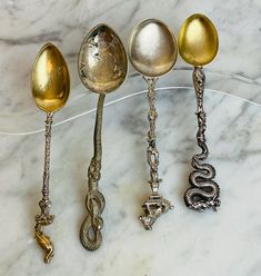 four spoons are lined up on a marble counter top, one is gold and the other silver