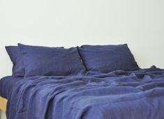 a bed with blue sheets and pillows on it's headboard, against a white wall