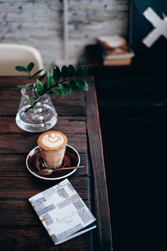 a cup of coffee sitting on top of a wooden table next to a vase with a plant