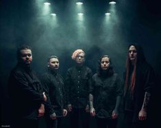 five men standing in front of spotlights with long hair on their heads and wearing black shirts