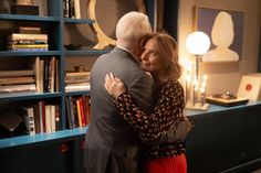 an older man and woman hug in front of a bookcase with books on it