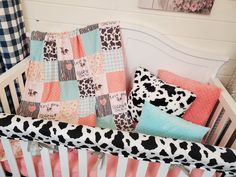 a baby crib with a cow print blanket and pillows on it's side