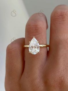 a woman's hand with a yellow gold ring and a pear shaped diamond on it