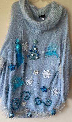 a blue sweater with sequins and snowflakes is hanging on a wall