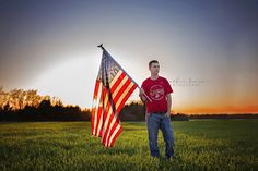 a man holding an american flag in the middle of a grassy field at sunset or dawn