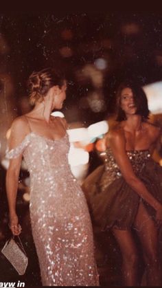 two women dressed in sequins walking down the street at night, one wearing a dress