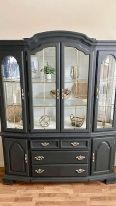 a black china cabinet sitting on top of a hard wood floor next to a potted plant