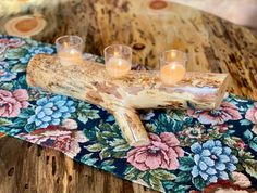 three votive candles are placed on a piece of driftwood with floral print fabric