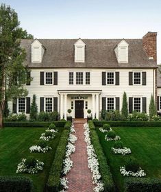 a large white house surrounded by lush green grass and bushes with flowers in the front yard