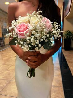 a woman in a white dress holding a bouquet of roses and baby's breath