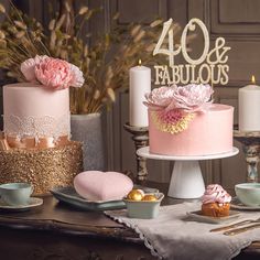 a table topped with two cakes covered in frosting and pink flowers next to candles