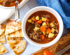 a bowl of soup with meat, potatoes and carrots next to sliced pita bread