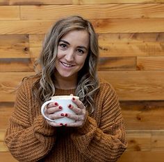 a woman holding a coffee cup in front of a wooden wall