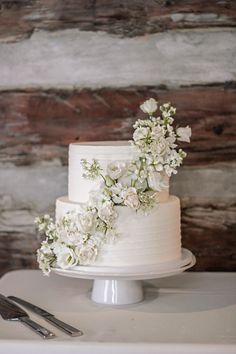 All white modern wedding cake with cascading floral design One Level Wedding Cake, Fireplace Wedding Flowers, Small White Wedding Cake, Wedding Cake Elegant Classy, Timeless Wedding Cake, Timeless Wedding Reception, Romantic Timeless Wedding, Single Tier Wedding Cake, All White Wedding Cake