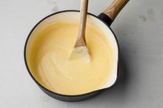 a wooden spoon in a saucepan filled with yellow liquid on a white counter top