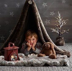 a little boy laying in front of a teepee tent with his teddy bear and lantern