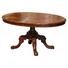 an oval wooden table with two leaves on one end and three legs, in the middle