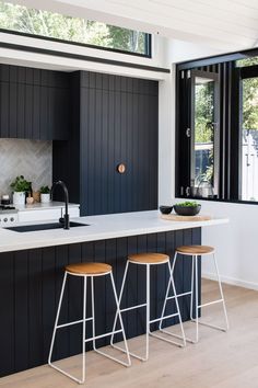 two stools are in front of the kitchen counter and bar area, with black painted wood paneling on the walls