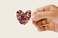 a hand holding up a heart shaped sticker with many people on it's face