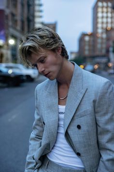 a man in a gray suit and white t - shirt is standing on the street