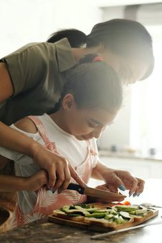 a woman helping a child cut vegetables on a cutting board