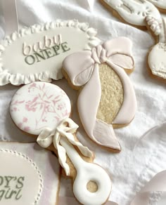 some decorated cookies are laying on a white table cloth with ribbons and tags around them