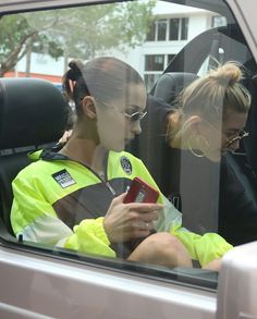 two women sitting in the back seat of a car looking at a cell phone together