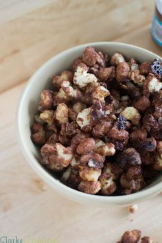 a bowl filled with chocolate covered popcorn sitting on top of a wooden table next to a bottle