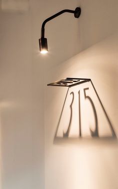 a wall mounted lamp with the number twenty five on it's side, next to a white wall