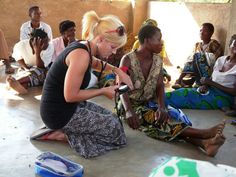 a group of people sitting on the ground in front of a wall and one woman is using a cell phone